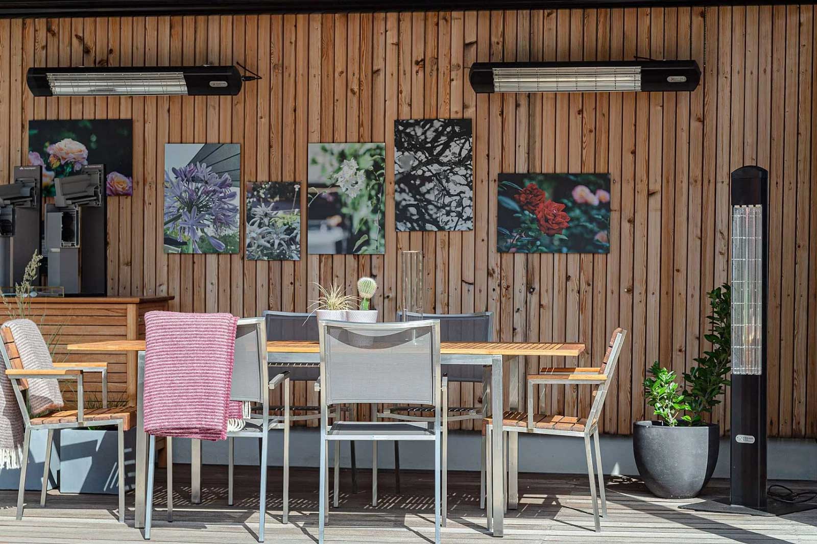 Drei Terrassendach Heat Tower, wovon zwei an einer Holzwand montiert sind und ein stehender vor der Holzwand.