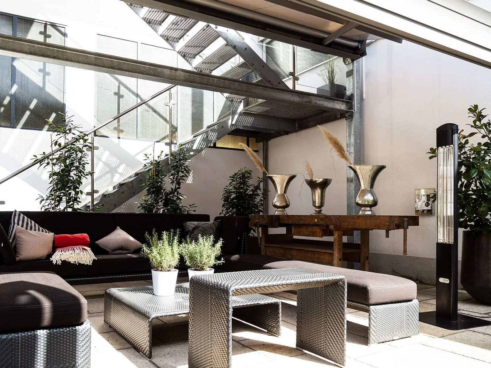 Ein schwarzer Heat Tower ideal für ein Terrassendach steht neben einer Bank mit Polsterauflage.
