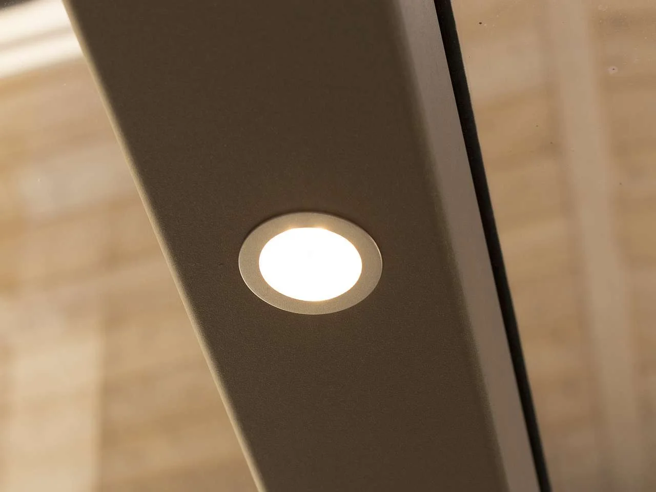 Eine runde LED Lampe in einer Querverbindung im Terrassendach verbaut.