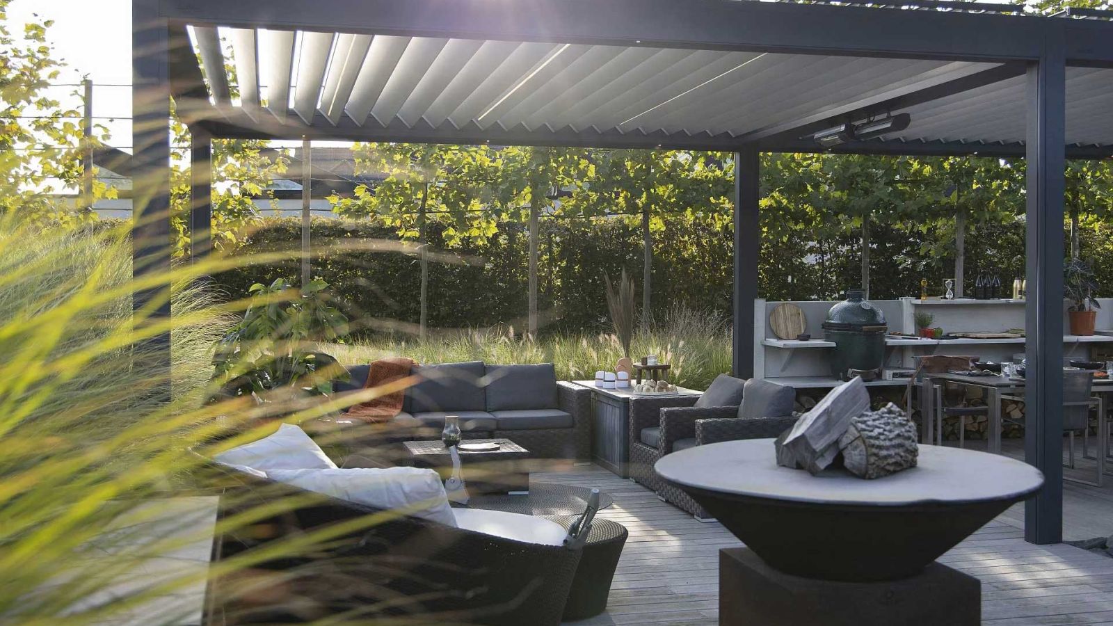 Ein Lamellendach in Ansbach mit Sitzgruppe darunter und verschiedenen Bäumen und Gräsern im Hintergrund.