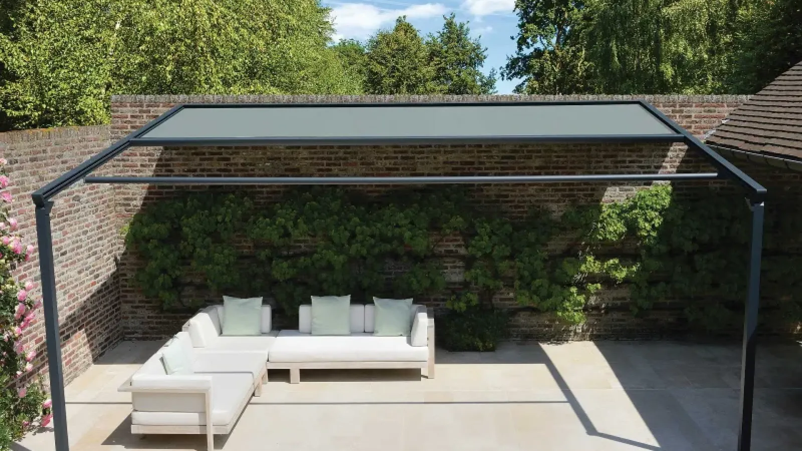 Eine schwarze Pergola Markise auf einer Terrasse mit einer hohen Wand im Hintergrund.
